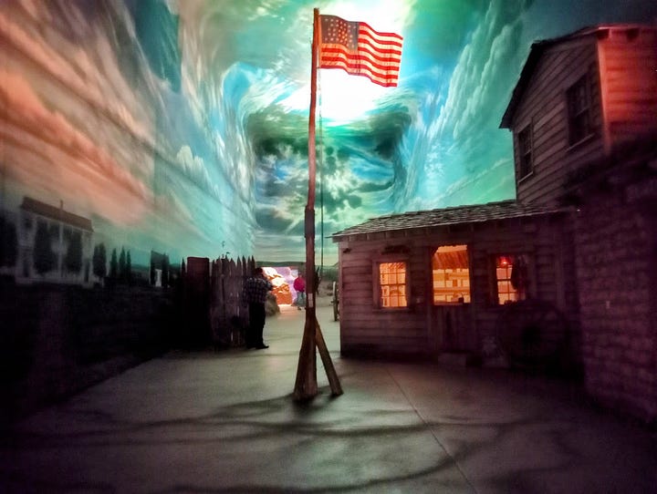 Photos showing log buildings and US flag on flagpole, swirly clouds and skies in high vaulted ceiling