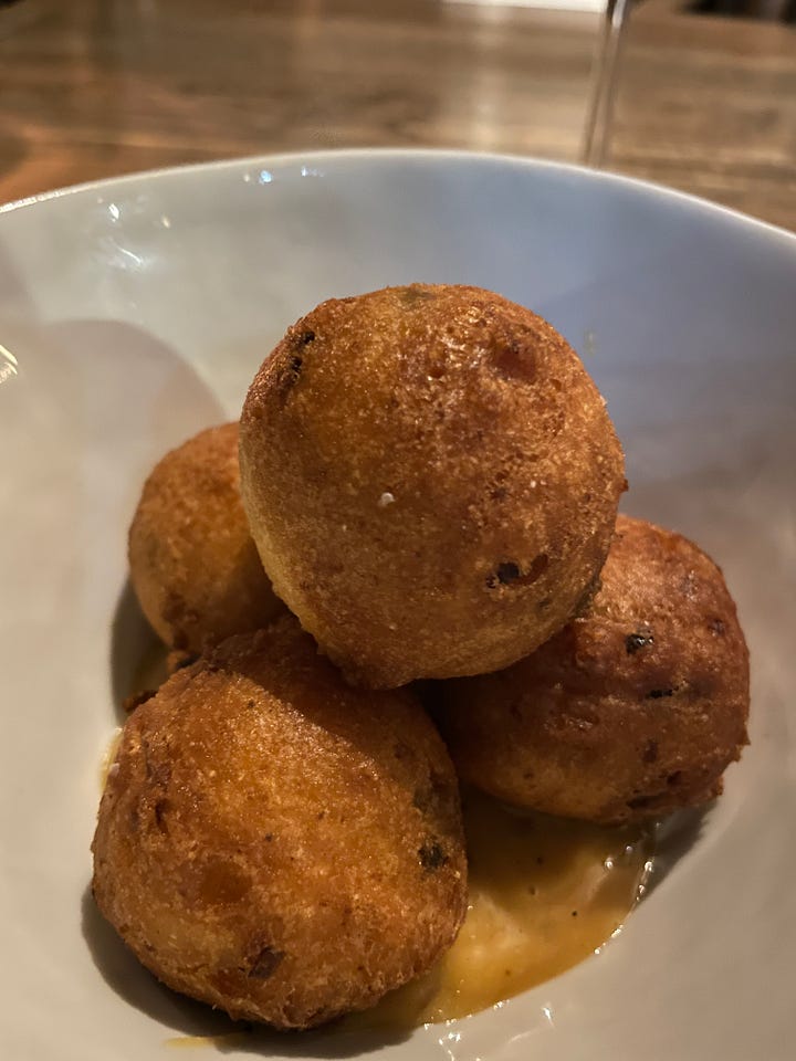 Bialy and dips, piece of lemon olive oil cake, hush puppies, a drink at a tropical-themed bar.