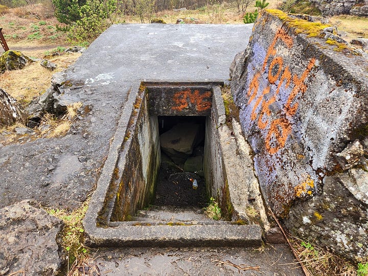 A concrete doorway into the hillside, and an open door leading straight down steps into an underground bunker.