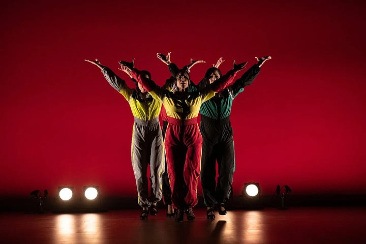 Two side-by-side images: On the left, against a red backdrop, three dancers in a V formation raise their arms to the sky, gazes lifted. They wear jumpsuits and flamenco shoes. On the right, against a black backdrop, one dancer reaches a palm upward as others gather around her, their hands resting on her torso and legs.