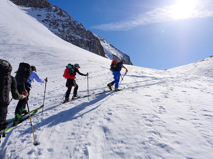 Images of people on ski tour, skinning up in a line behind each other, approaching a mountain hut.