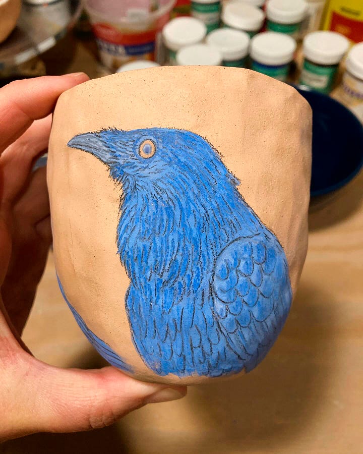 two pinch-pot cups, both with vibrant blue/purple ravens drawn/painted on them