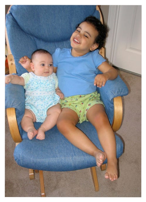 baby and young child together in a blue chair, Valeries's family smiling and wearing red and black.
