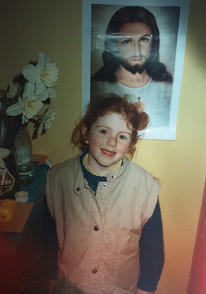 A young red-headed child making her first Holy Communion and standing next to a vase of droopy Daffodils in front of an image of Jesus Christ