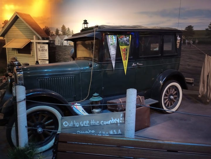 Photo of car driving through extremely deep mud, Model T car from 1920s,Info panel, Model T with mural of motor court behind, mural and tableau of motor court cabins