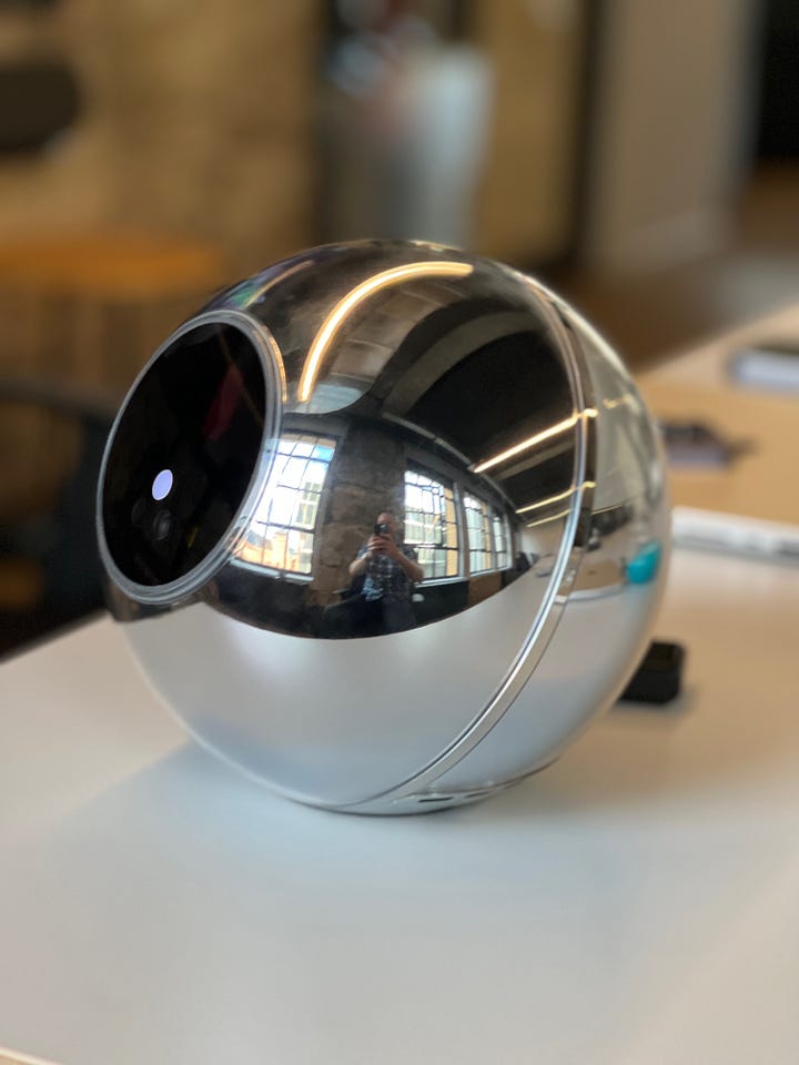 A red camera lens, depicting the HAL 9000 AI from Space Odyssey, and a photograph of a spherical chrome object with a lens (the Worldcoin Orb)