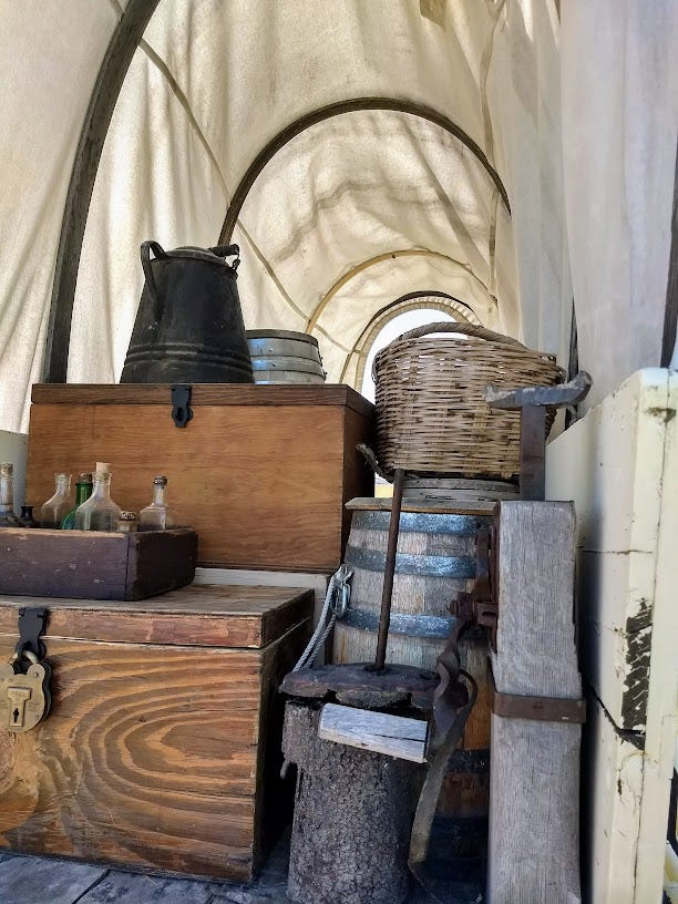 Inside of covered wagon, filled with boxes, coffee pot,, and baskets. Other photo shows glass bottles in box