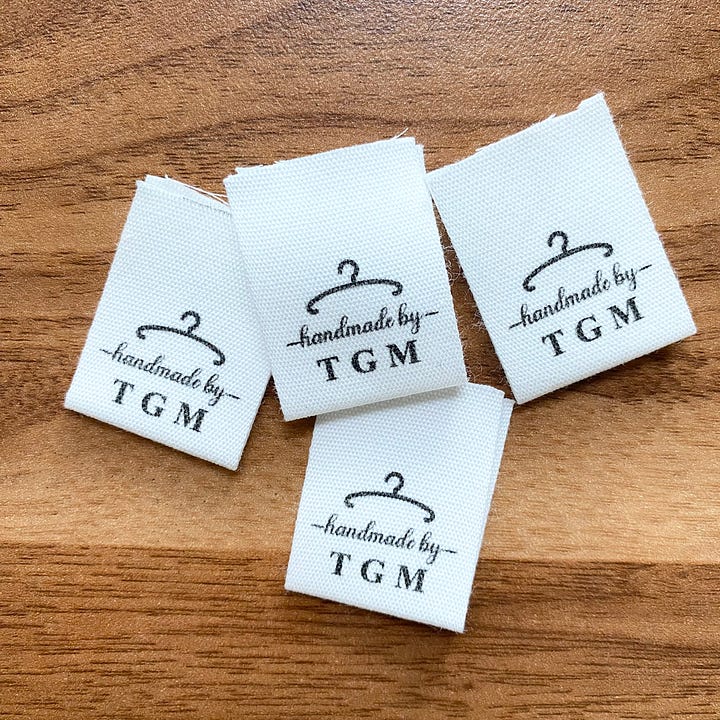 Left image of 4 fabric tags on a wooden table. Fabric tags read "handmade by TGM". Right image of fabric tag sewn into shirt collar.