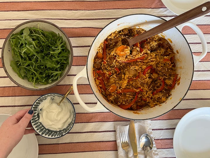 A photo of cookbooks on a shelf with Post-It tabs sticking up from the pages; a view of an onigiri mold with rice and salmon inside; a table with a pot of kabsa, a bowl of greens, and a small bowl of yogurt; a view of a pan with cooked harissa chickpeas and pieces of feta.