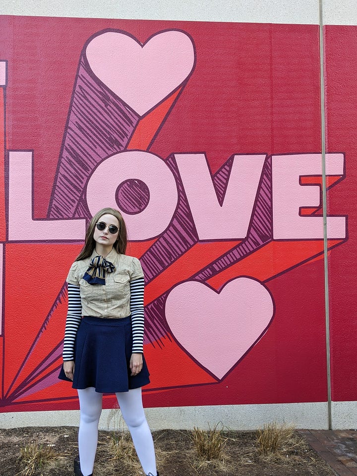 4 photos of me as M3gan at The Domain. M3gan drinking bubble tea, M3gan in front of a "LOVE" mural, M3gan in front of the Apple store, and M3gan looking into the Coach store.