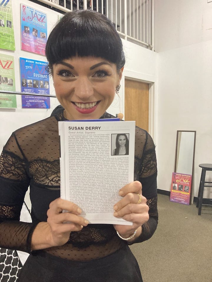 Susan Derry as The Witch in a wire and leaf headdress mask; Cree Carrico in  concert dress holding a program with Susan Derry's bio in it.