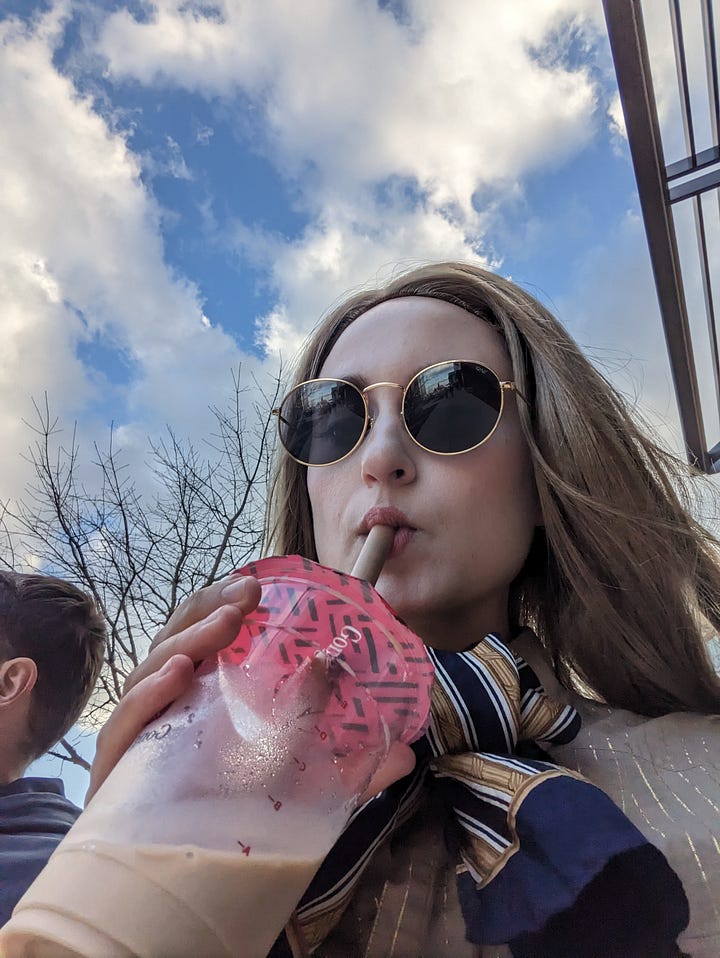 4 photos of me as M3gan at The Domain. M3gan drinking bubble tea, M3gan in front of a "LOVE" mural, M3gan in front of the Apple store, and M3gan looking into the Coach store.