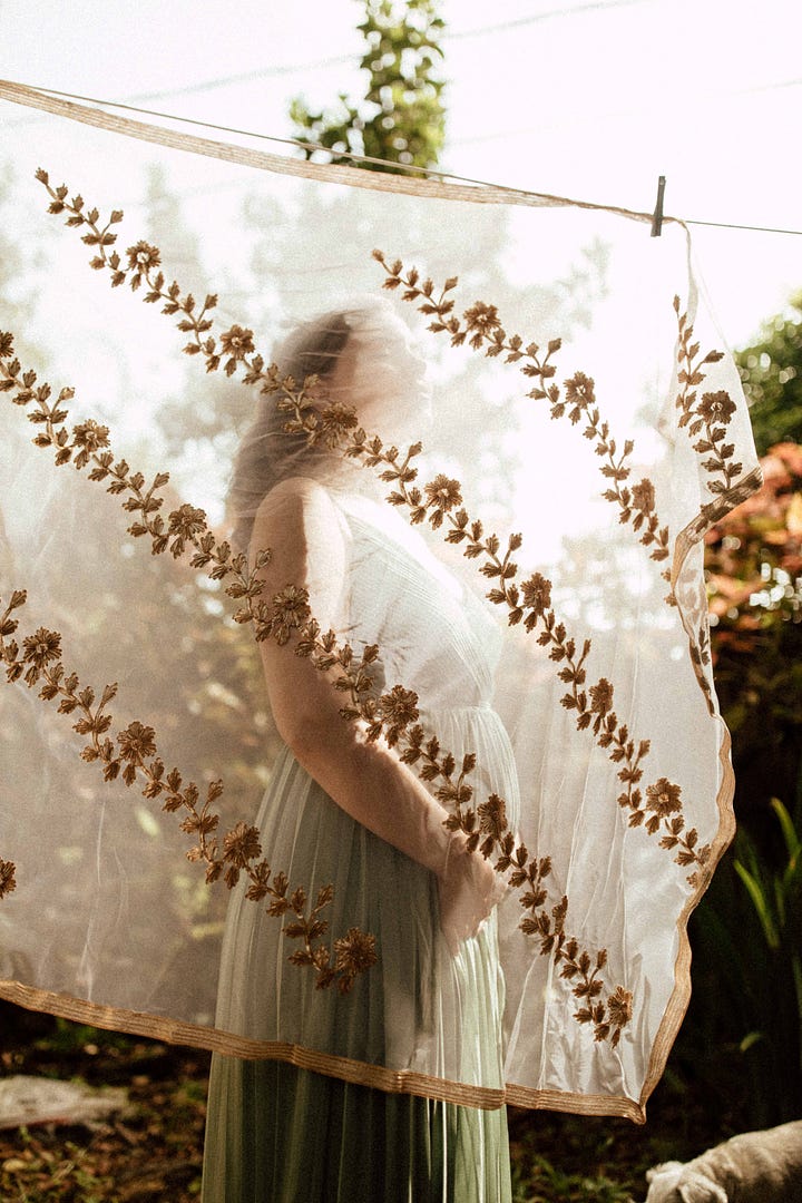 Four photos in shades of greens and coppers and gold, depicting Ganga Devi 6 months pregnant in a sage green gown surrounded by copperleaf plants and gold brocade fabric. In the background of the final photo, etched glass reads the lines from Stanley Kunitz: "The Universe is a continuous web, touch it at any point and the whole web quivers.""
