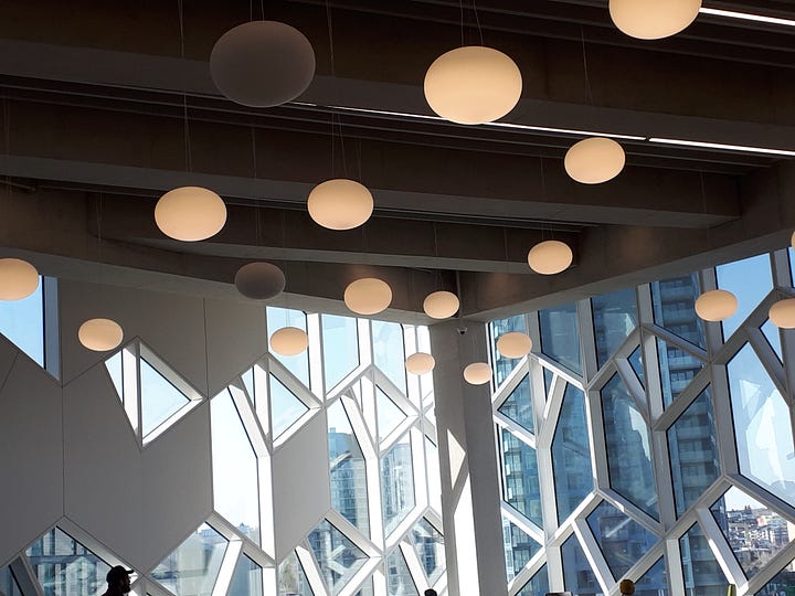 Calgary library. Wooden roof structure; lights and windows; sunset shining in through a large window; LRT trains running under the building.