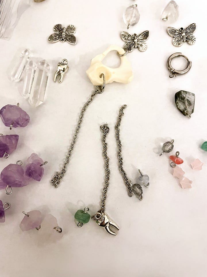 Overhead view of a table with animal bones, crystals, beads, cable chain, and jewelry hardware.