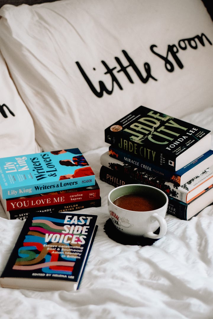Stack of paperback books on a cosy white duvet, with a cup of coffee.