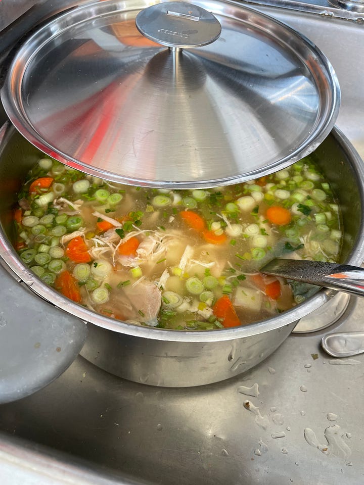 A positive covid test rests on a wooden table.  A delicious pot of chicken soup with the lid partly off.