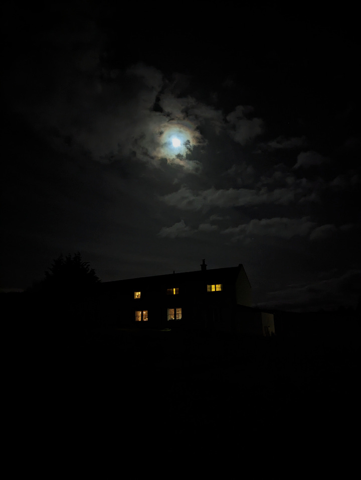 Image one is a photo of Moniack Mhor main house, a dark silhouette against the light of a full moon. The second is a photo of the living room fire, glowing multi-coloured from salt-coated pine cones.