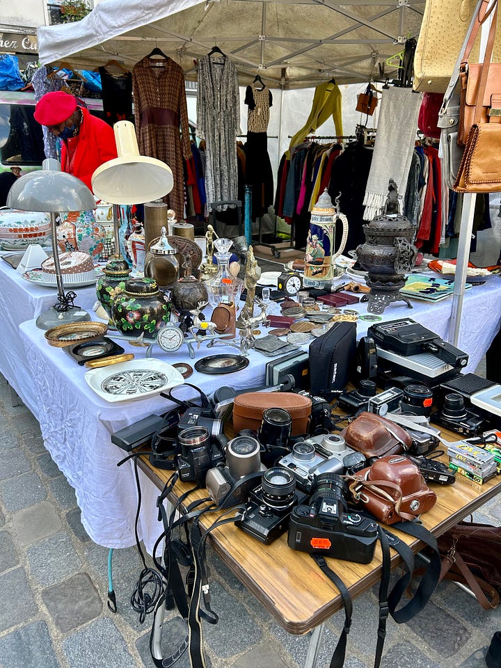 Flea market clothes, shoes, cameras, vintage tableware displayed on tables an an outdoor market
