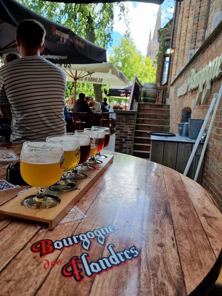 Photo 1: Tasting paddle at Brewery Bourgogne des Flandres with church in the background. Photo 2: Bruges Grote Markt with a horse pulling a buggy entering the photo from left. Photo 3: view from the Lovers Bridge. Photo 4: close up of the New Parrot windmill. 