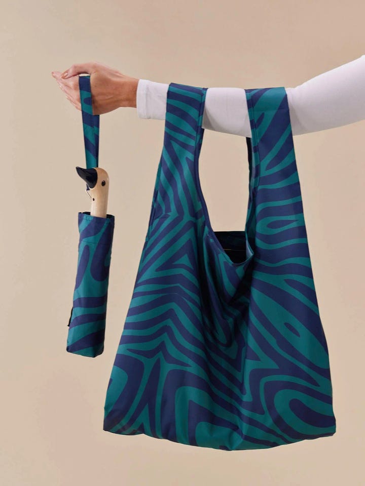 Blue umbrella and matching reusable bag, each with a swirling blue pattern. Crafted from recycled plastic, these items add a vibrant pop of color while promoting sustainability.