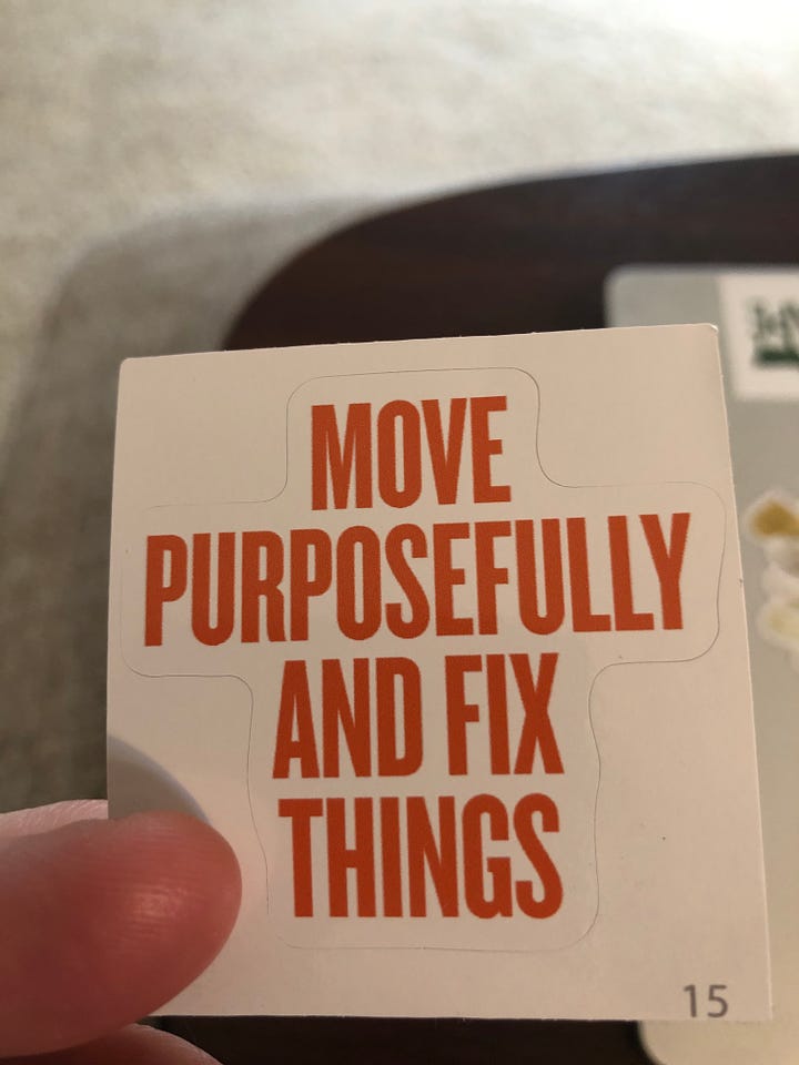 white sticker with orange text that says "move purposefully and fix things"; second picture of silver laptop with sticker on it
