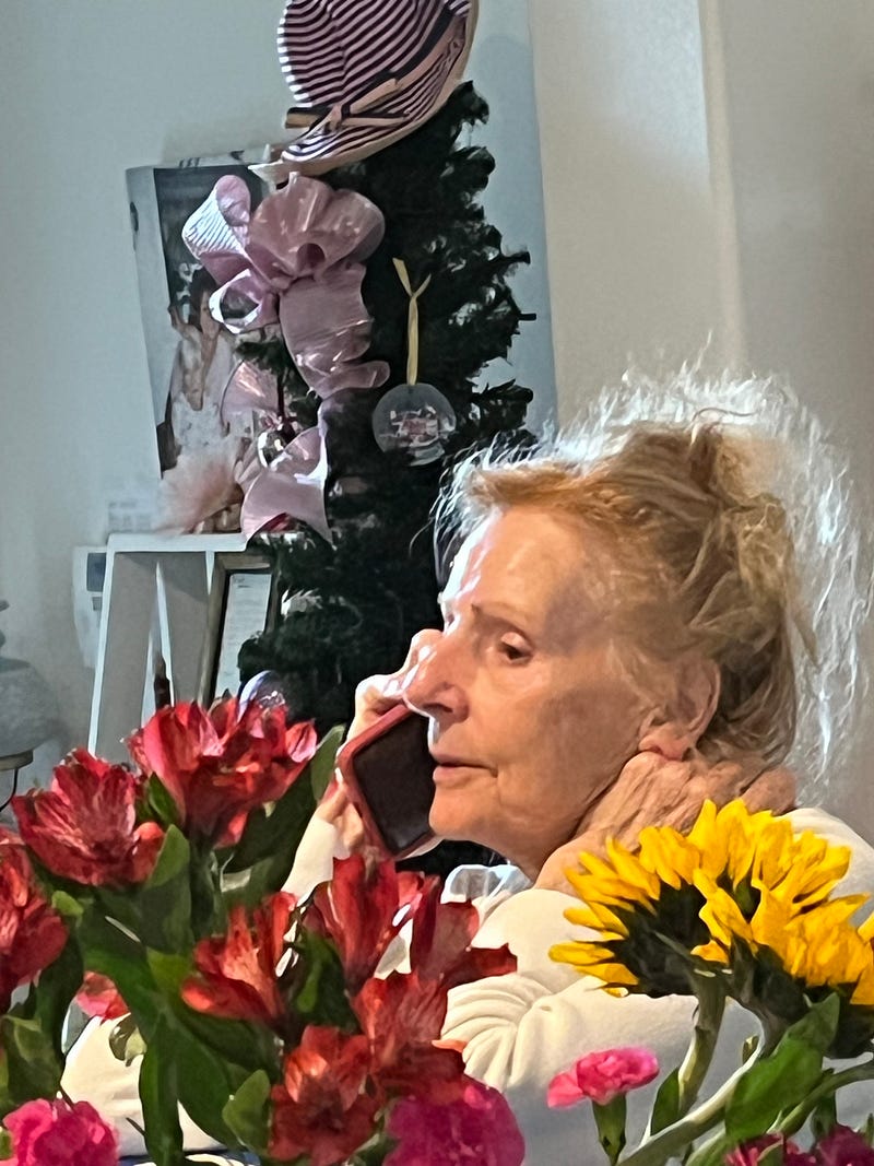 Kailee's Nana on the phone, beside bright red and yellow flowers