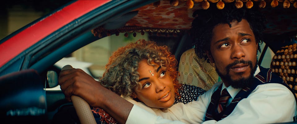 Film still: a man in a shirt and tie drives a car with a tasseled ceiling while a woman rests her head on his shoulder